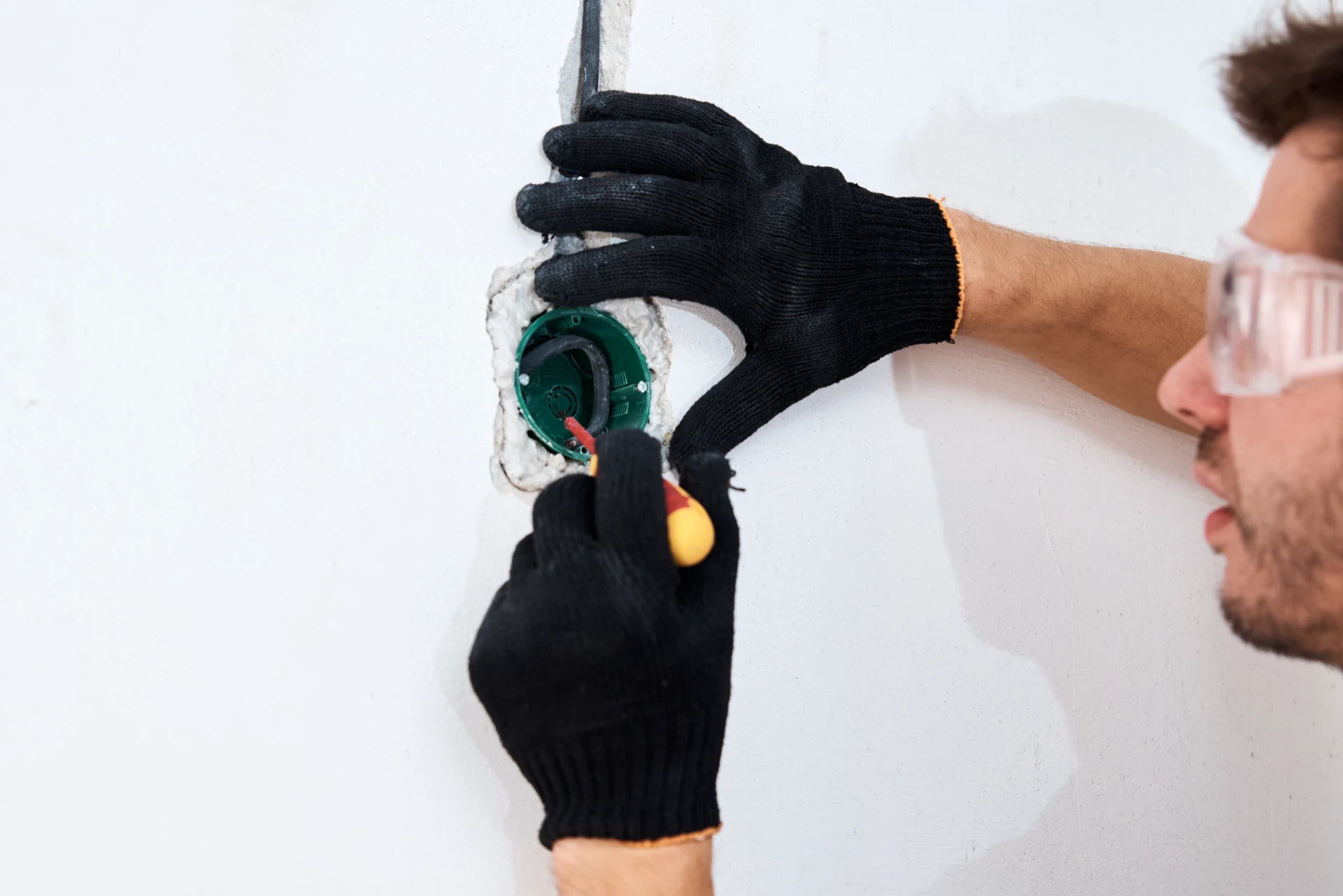 Elektriker installerer eludstyr på væg med værktøj og beskyttelsesbriller.