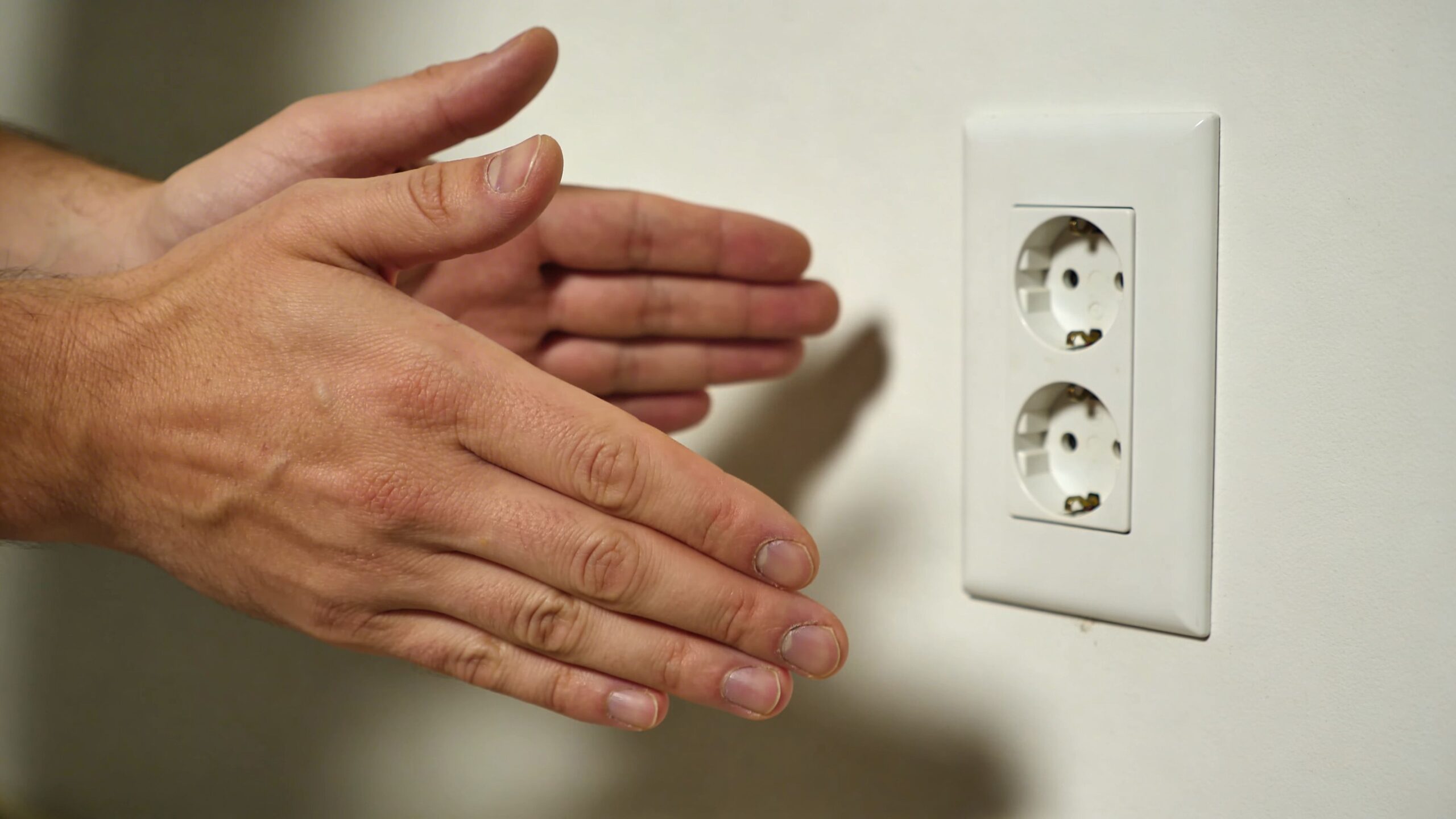 En person peger mod en dobbelt stikkontakt på en hvid væg for at illustrere elektriske installationer.