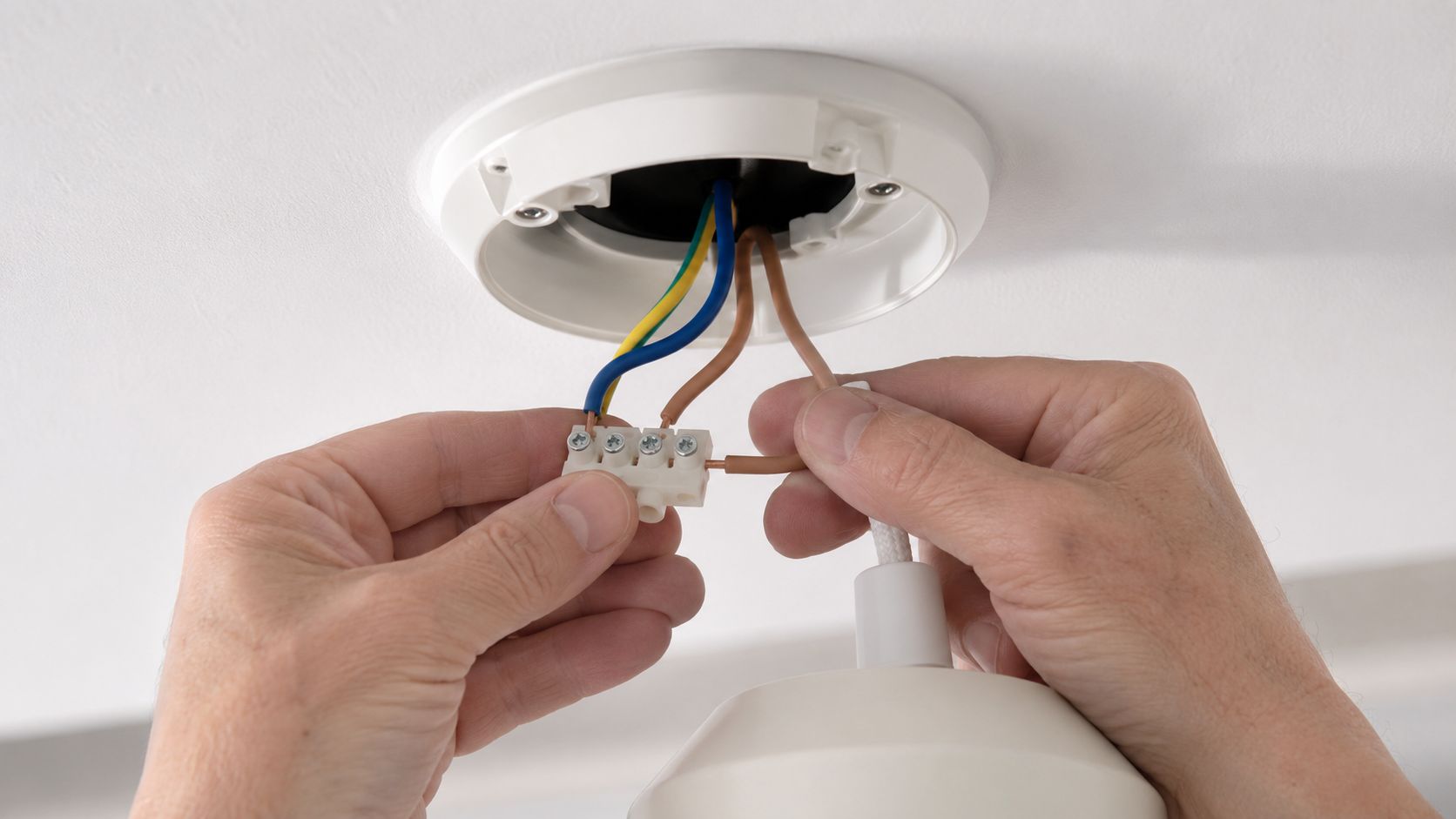 En person installerer en lampe ved at tilslutte elektriske ledninger i et stik på loftet.